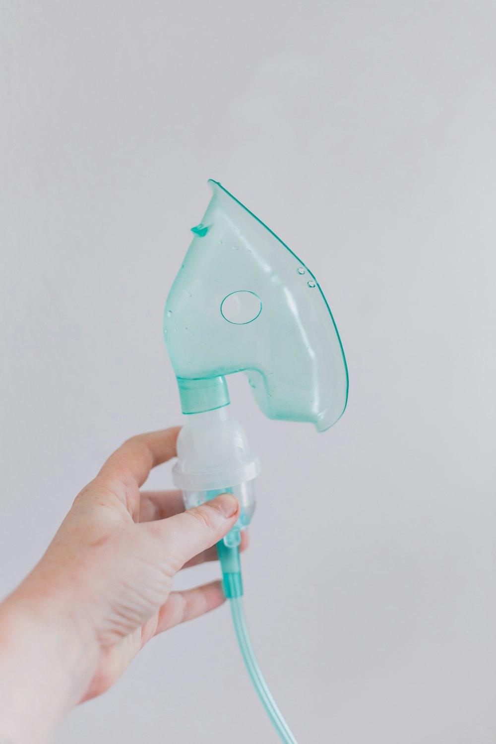 A hand holding a clear nebulizer mask against a pale background