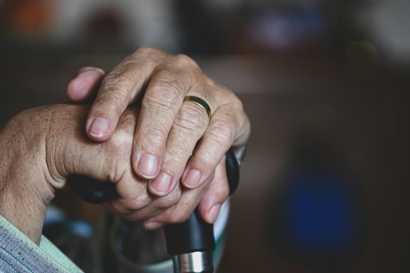 Older hands with a ring resting on the handle of a walking cane