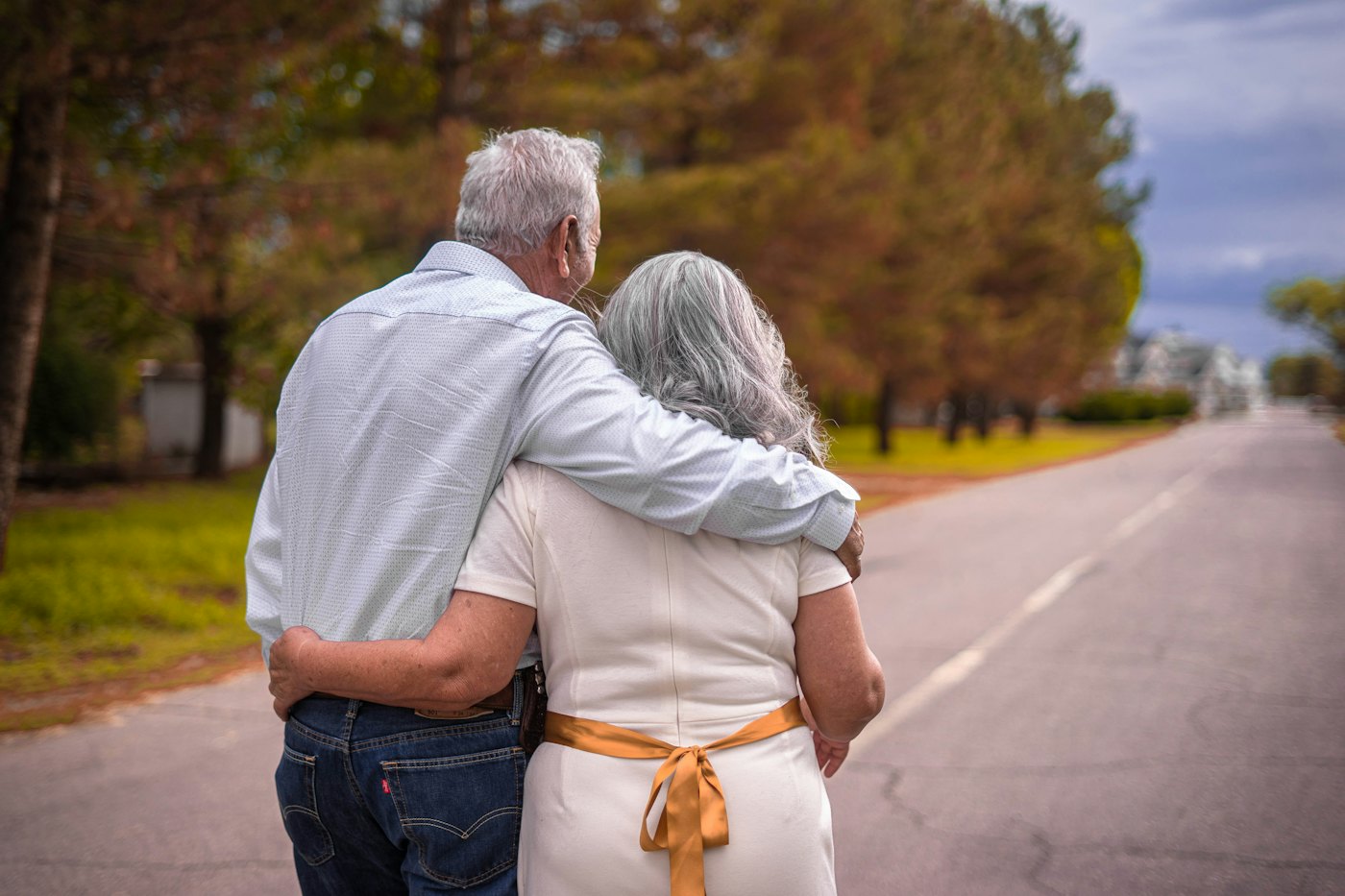 An older couple walking arm in arm down a country road