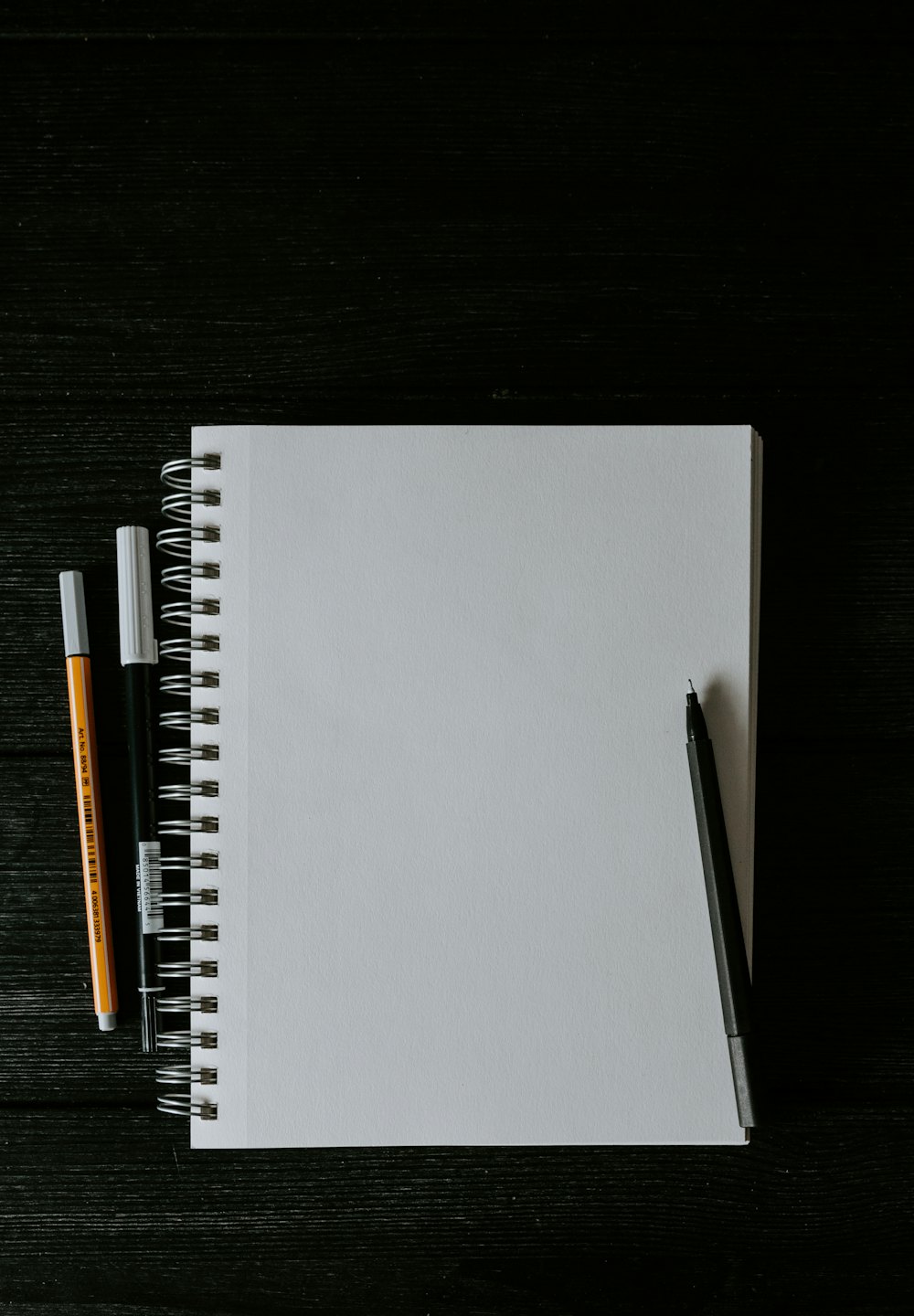 A spiral notebook and an orange pen on a white desk
