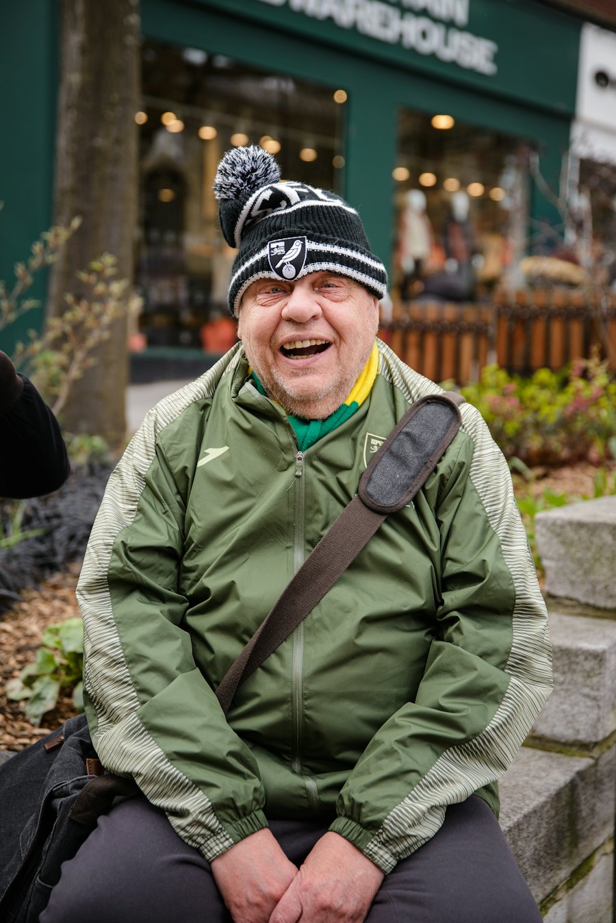An older man in a cap and jacket laughing outdoors